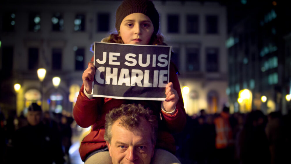 Ein Kind hält am 7. Januar das Solidaritätssymbol „Je suis Charlie” in den nächtlichen Himmel Brüssels