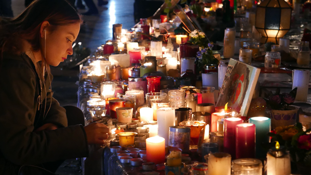 Ein junges Mädchen kniet vor dem Kerzen- und Blumenmeer einer Straßenecke an der Rue Bichat nieder. Hier ermordeten am 13. November einige der Attentäter von Paris viele Restaurantbesucher.