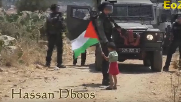Ein kleiner palästinensischer Junge gibt einem israelischen Soldaten die Hand. Im Hintergrund schreit der Vater des Kleinen, er solle Steine auf den Soldaten werfen.