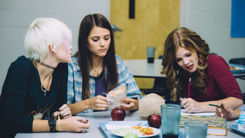 Rachel (Masey McLain) sitzt zwischen ihren beiden Freundinnen in der Cafeteria der Columbine-High-School