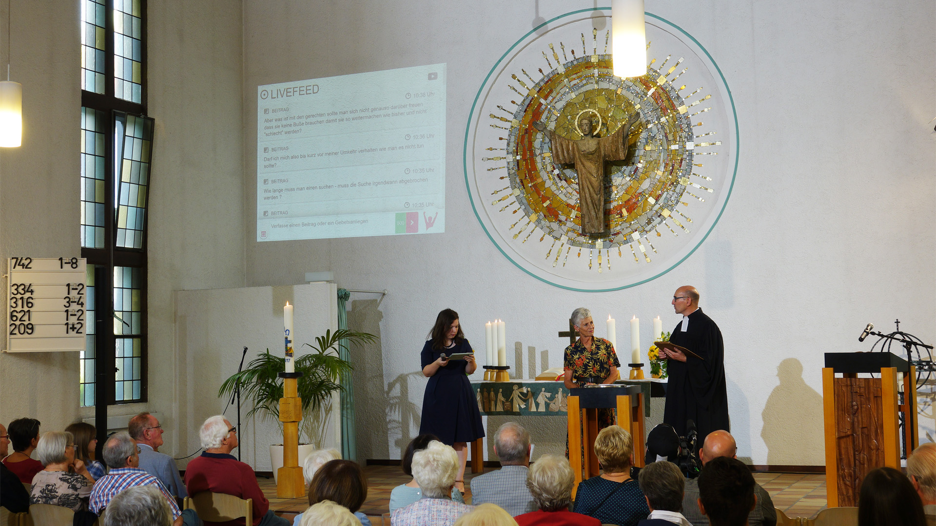 Moderatorin Laura Schäfer (li.) führt liturgisch durch den Gottesdienst, Wendy Schröder und Rasmus Bertram führen das Predigtgespräch. Beiträge von den Online-Besuchern des Gottesdienstes sowie Lied- und Bibeltexte, werden an die Kirchenwand projiziert.