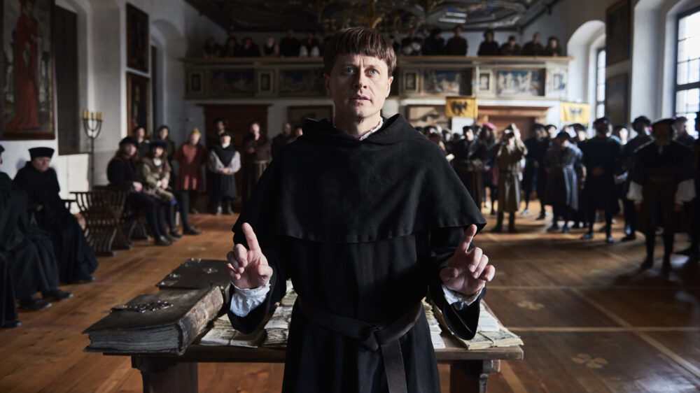 "10 Tage im April": Roman Knizka in der Rolle des Martin Luther steht in Worms an einem Tisch mit Schriften.