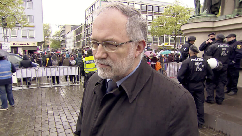 Joachim Kuhs, AfD-Kandidat in Baden-Baden, kann nur unter Polizeischutz auftreten. Der SWR-Reporter unterstellt deswegen, der Politiker inszeniere sich als Opfer.