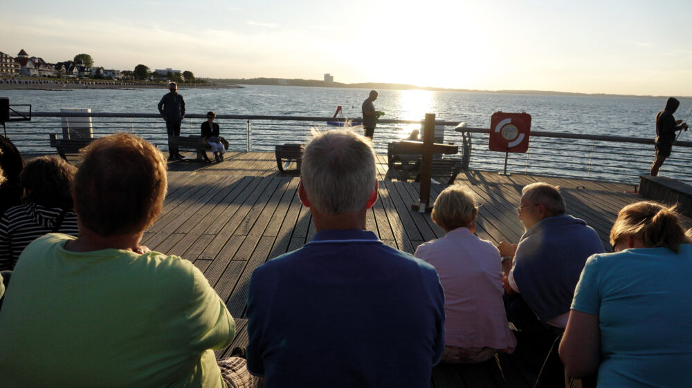 Auf der Seebrücke versammeln sich Einheimische und Touristen zur abendlichen Andacht um ein Kreuz