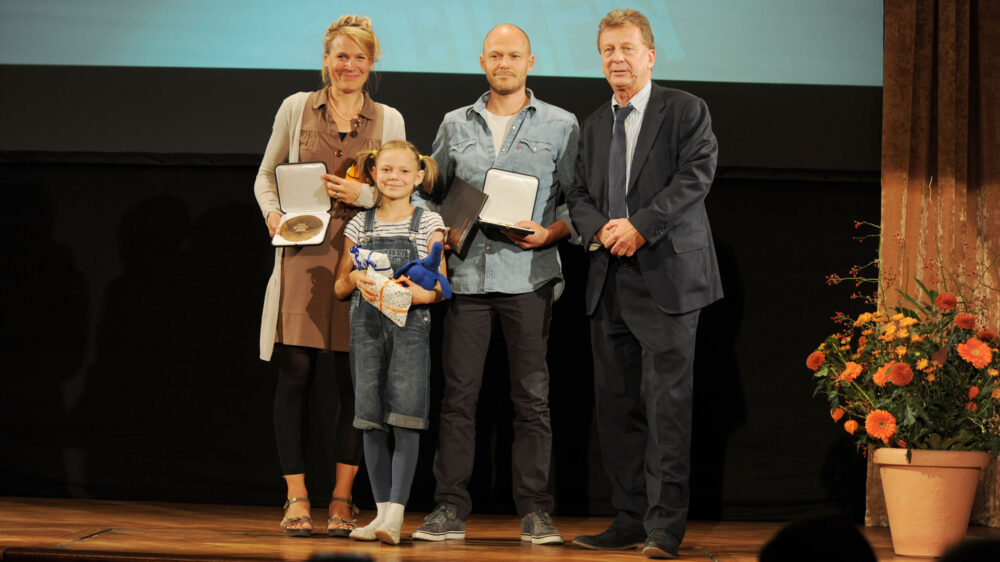 Die Evangelische Kirche zeichnete den Beitrag „Planet Willi – Die Sendung mit dem Elefanten“ von Birthe Müller-Wittkuhn (l.) und Matthias Wittkuhn (2.v.r.) mit Tochter Olivia und Pfarrer Bernd Merz (r.) mit dem „Robert Geisendörfer Preis“ aus. Nicht im Bild ist ihr Sohn Willi, der das Downsyndrom hat.