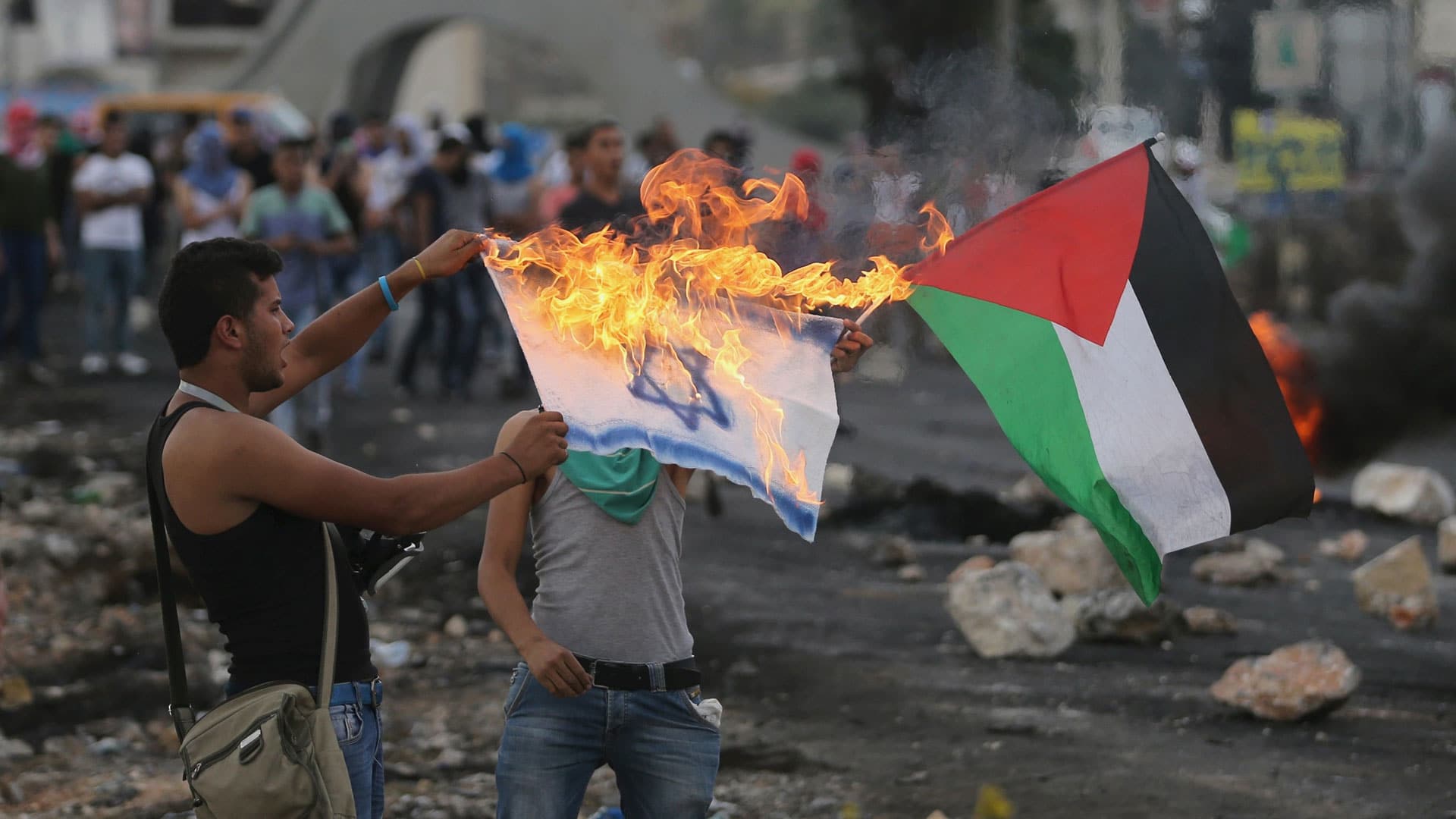 „Warum wir hassen: Fremde“: Zwei Männer halten eine brennende Israel-Flagge und schwenken parallel eine Palästina-Fflagge.