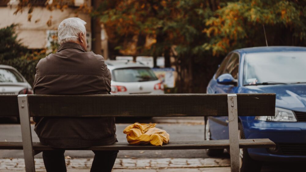 Älterer Mann sitzt auf Parkbank