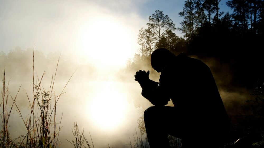 Ein Mann betet draussen vor einem See