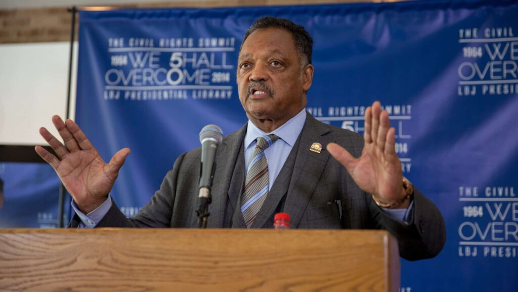 Der Bürgerrechtler und Bapistenpastor Jesse Jackson am Rednerpult. Im Hintergrund steht auf einem Transparent: „We Shall Overcome“