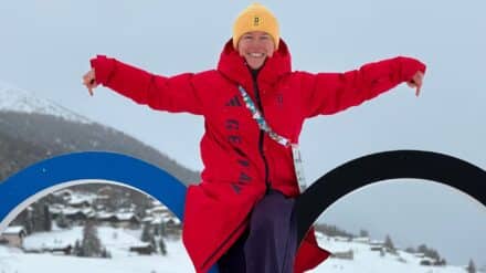 Freestyle-Skierin Emma Weiß in einer roten Winterjacke zwischen zwei Olympia-Ringen