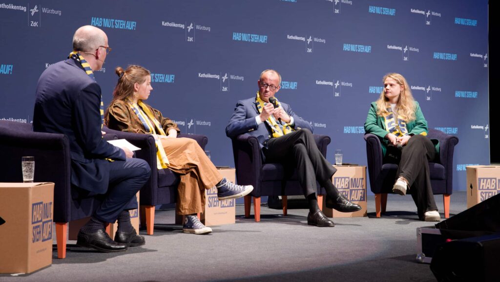 Bundeskanzler Friedrich Merz im Gespräch mit jungen Menschen. er sitzt auf einem schwarzen Sessel.