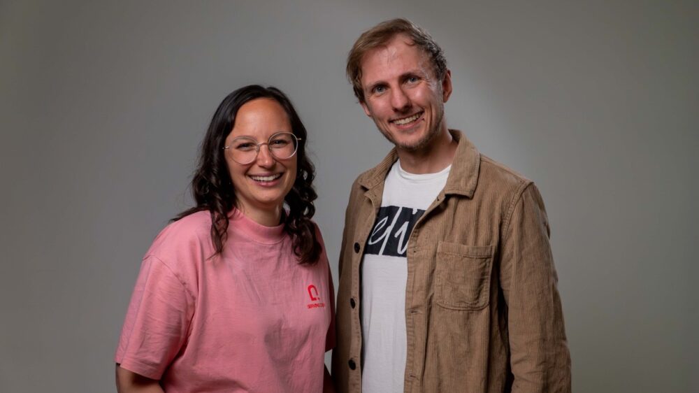 Dina Ketzer und Pierre-Schwering in der Halbtotalen, sie lächeln freundlich in die Kamera