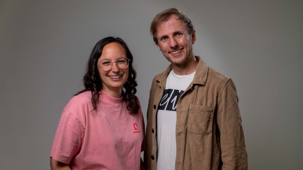 Dina Ketzer und Pierre-Schwering in der Halbtotalen, sie lächeln freundlich in die Kamera