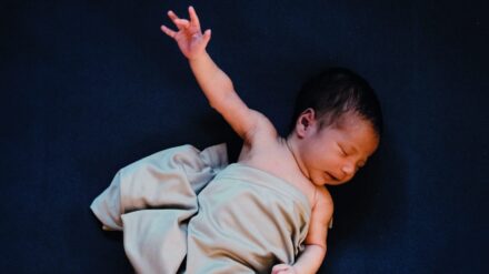 Baby in ein Tuch gewickelt vor dunklem Hintergrund